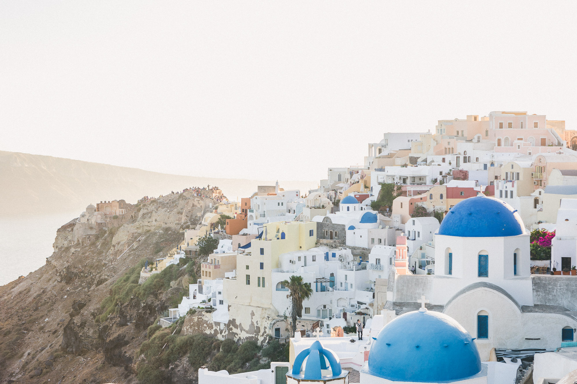 A stunning view of Santorini, Greece, featuring white-washed buildings with blue domes overlooking the Aegean Sea, under a clear sky.